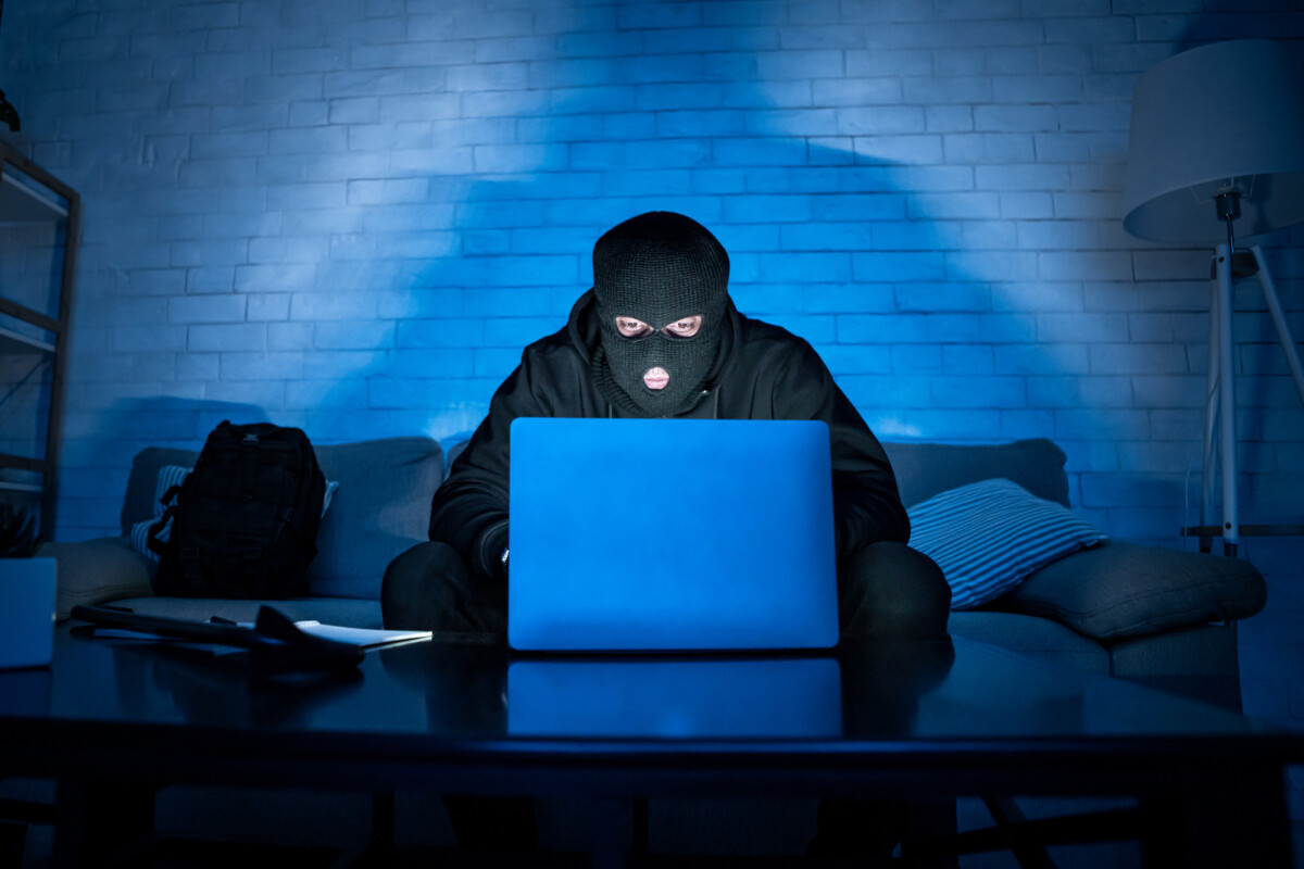 Masked hacker downloading private information using pc